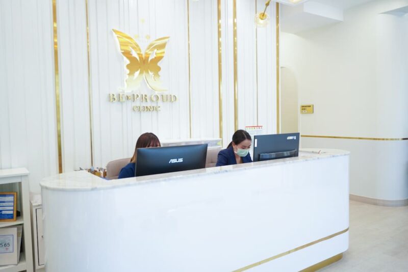 เคาน์เตอร์ต้อนรับของบีพราวด์คลินิก ปัจจุบัน แสดงพนักงาน 2 ท่านพร้อมโลโก้ผีเสื้อสีทองด้านหลัง