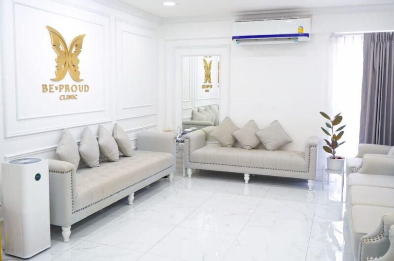 ห้องรับรองลูกค้าบีพราวด์คลินิก ปัจจุบัน โซฟาสีเทาอ่อนพร้อมโลโก้ผีเสื้อสีทอง แสดงบรรยากาศที่หรูหรา สะอาด และสะดวกสบายดุจบ้าน